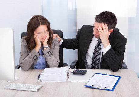 Worried Businessman And Woman Calculating Bills At Desk In Office